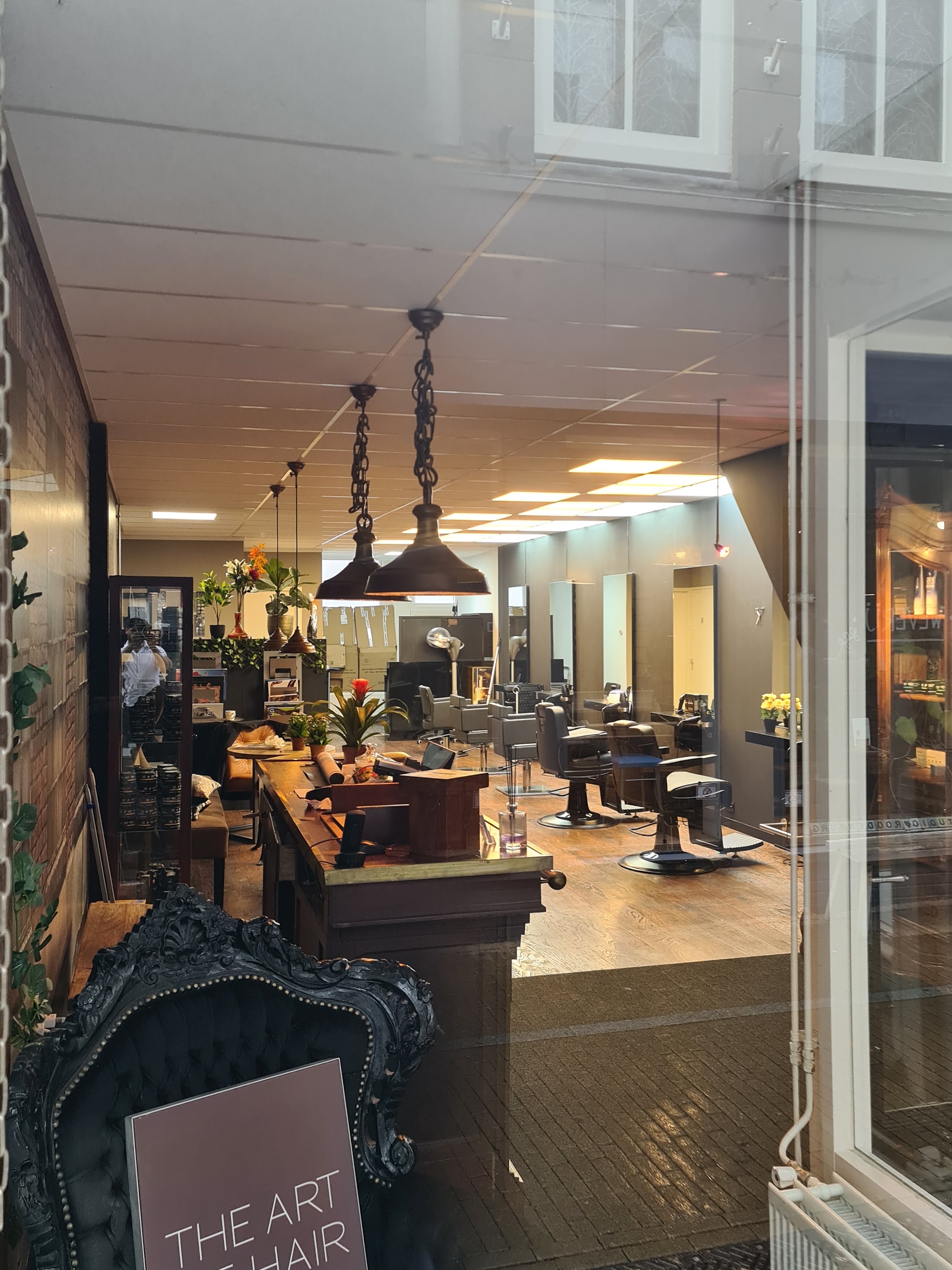 Blik door het raam in de salon van The Art of Hair, met het bordje The Art of Hair op de voorgrond